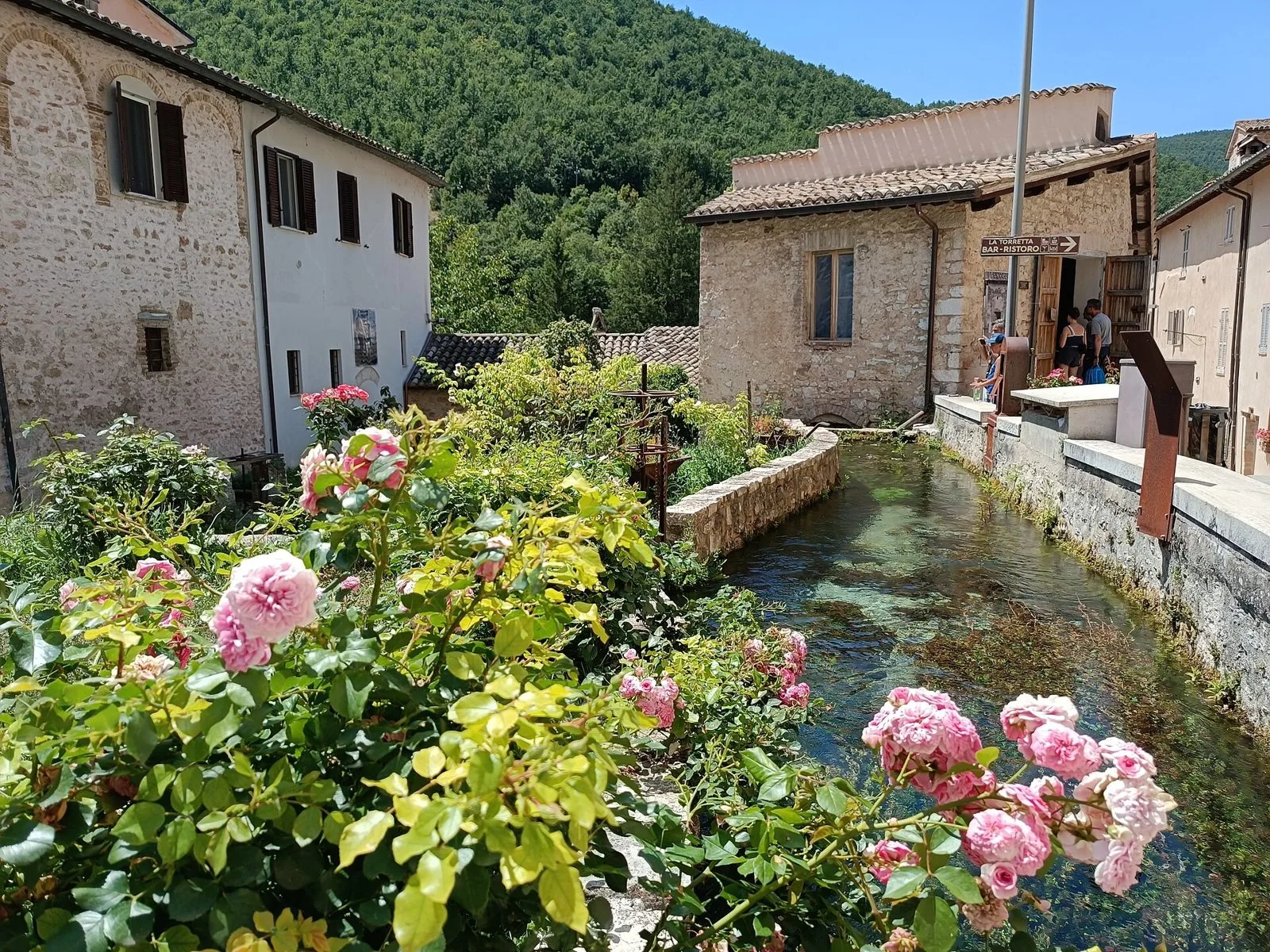 Canale d'acqua limpida tra case in pietra e rose in fiore a Rasiglia in estate